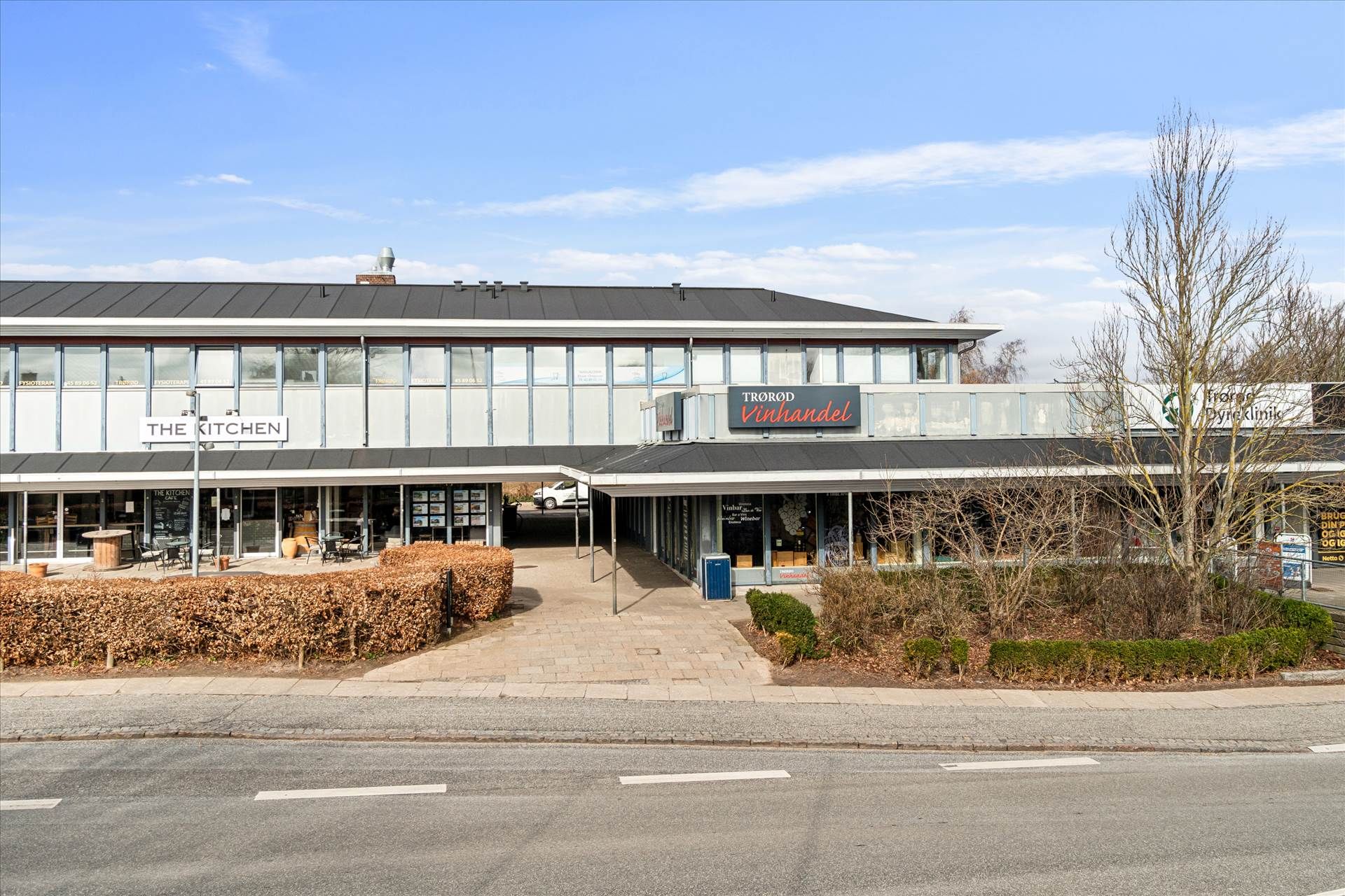 Et kommercielt bygningskompleks med butikker, The Kitchen, Trøø Vinhandel og Brugsen. En stor parkeringsplads foran med