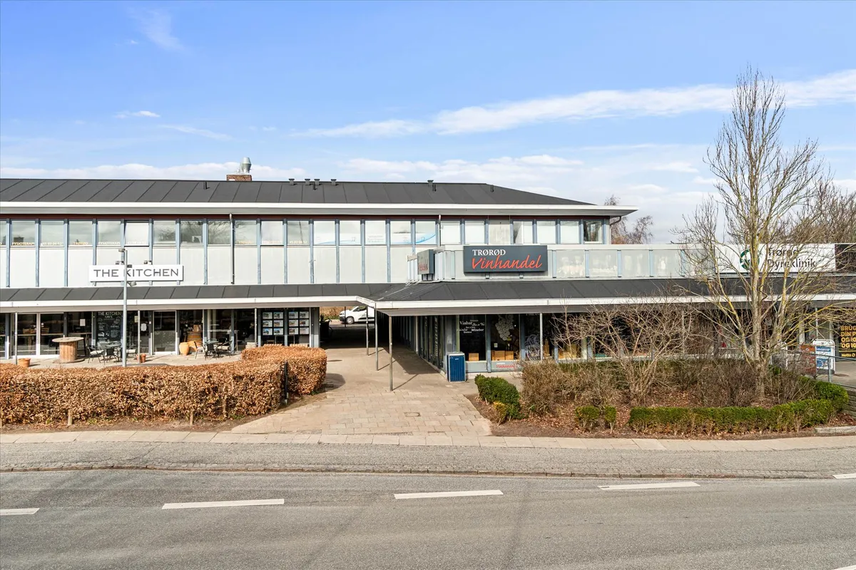 Et kommercielt bygningskompleks med butikker, The Kitchen, Trøø Vinhandel og Brugsen. En stor parkeringsplads foran med