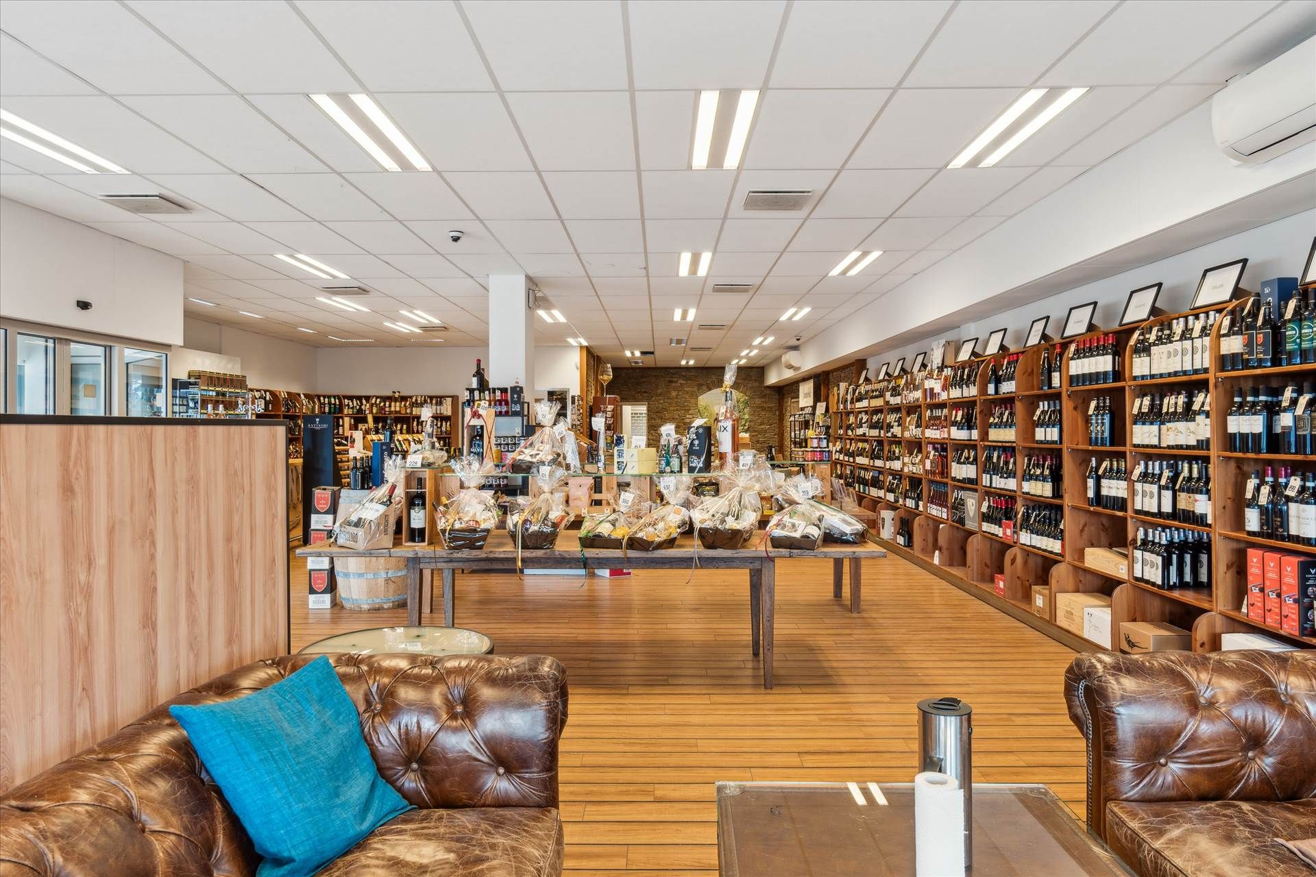 Inde i en vinforretning med smukke lædersofaer og trægulve, hvor flere vinflasker og vinkurve står på et langt bord og flere