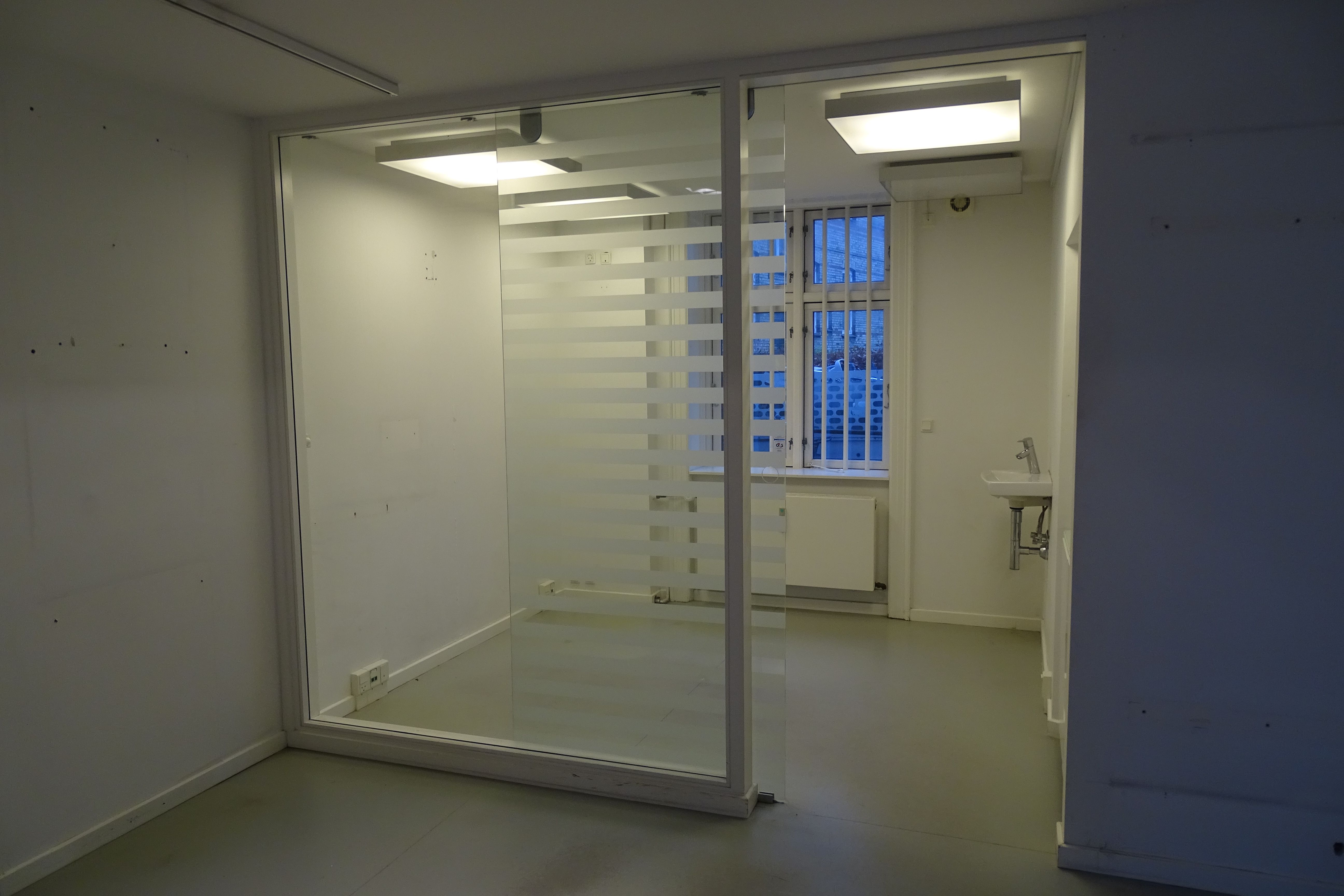 Lys og moderne kontorrum med glasdør, hvid væg, hvidt toilet, hvide loftsbelægninger og lysekroner