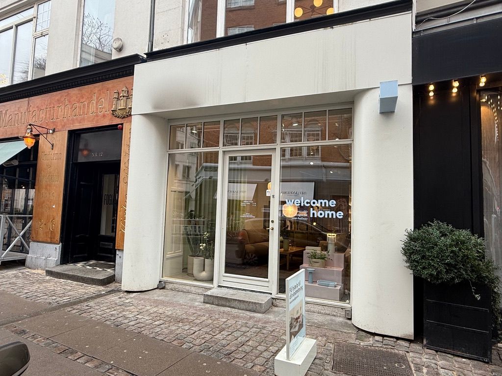 Butik med velkomstskiltet, der læser welcome home og udstillingsvinduer med interiør og plante.