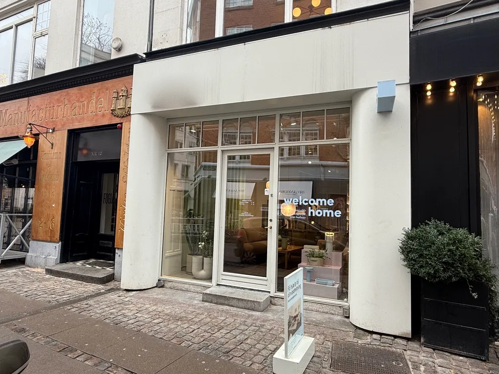 Butik med velkomstskiltet, der læser welcome home og udstillingsvinduer med interiør og plante.