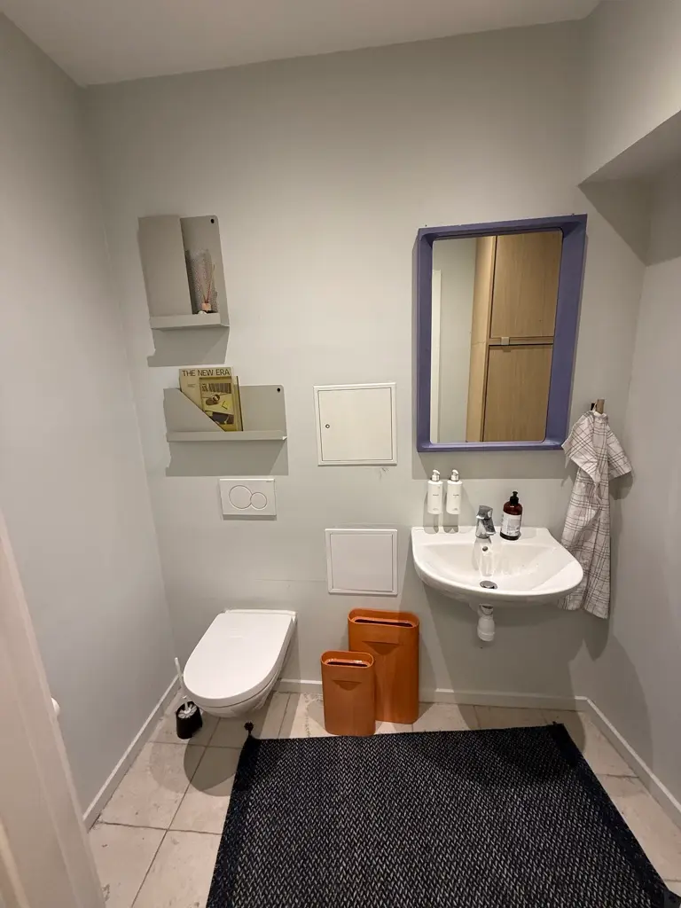 Toiletrum med hvid toilet, hvidt vask og brusekabinet, to toiletpapirruder og to toiletpapirruder, der er hængende på væggen