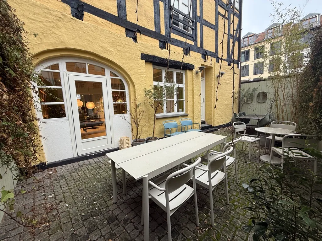 En terrasse med hvide stole og borde, en gul mur og plantager med grønne planter