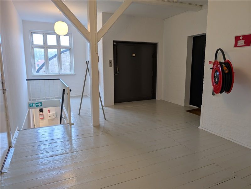 Her ses en stor og pæn indgangshal til et kontor med hvide vægge og gulv og en lyse pære i loftet