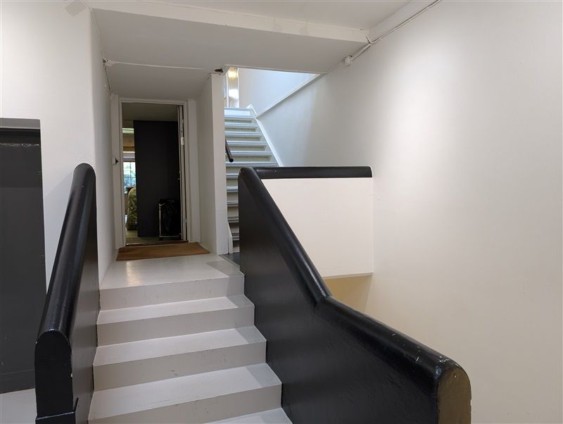 Moderne trappe med hvide trappetrin og sort metalgevær. Trappen er i et hvidt rum med højt til loftet og lyse loftsvinduer