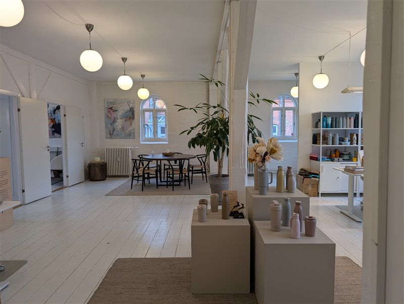 Kontor med bord, stole, lysekroner, plante, og flere ting på høj hylde og gulv