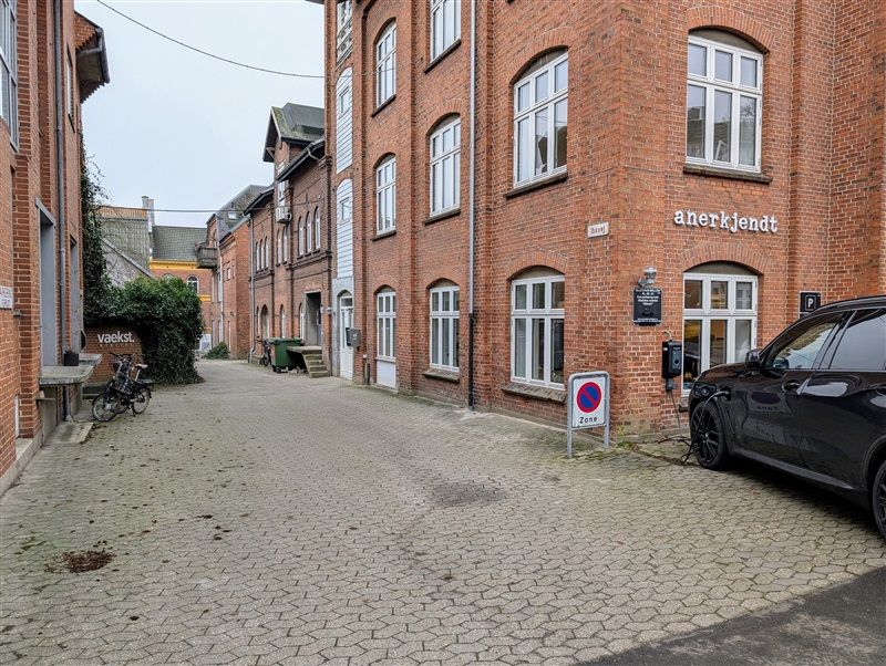 Lejlighedspark med røde mursten og kørestue med parkeringszoneskilt og elbilopladestation foran