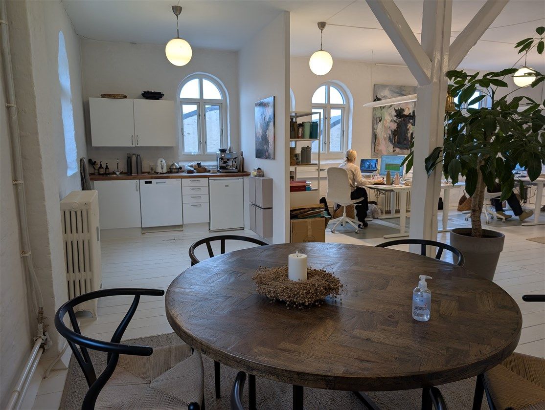 Et kontor med hvide vægge, runde vinduer, højt loft, møbler og en person sidder ved et bord