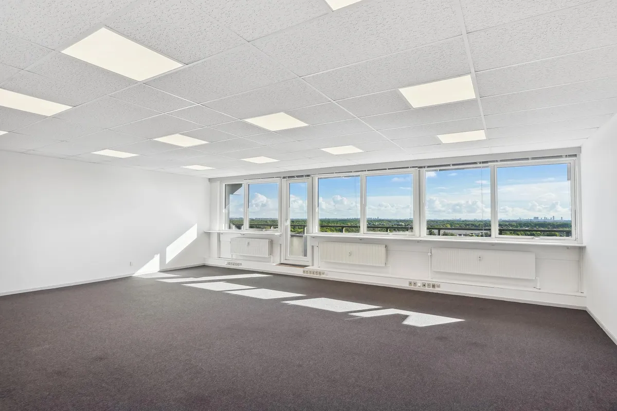 Moderne og rummelige kontor med højloft, lyse gulvbelægning, hvide vægge og store vinduer med udsigt over byen