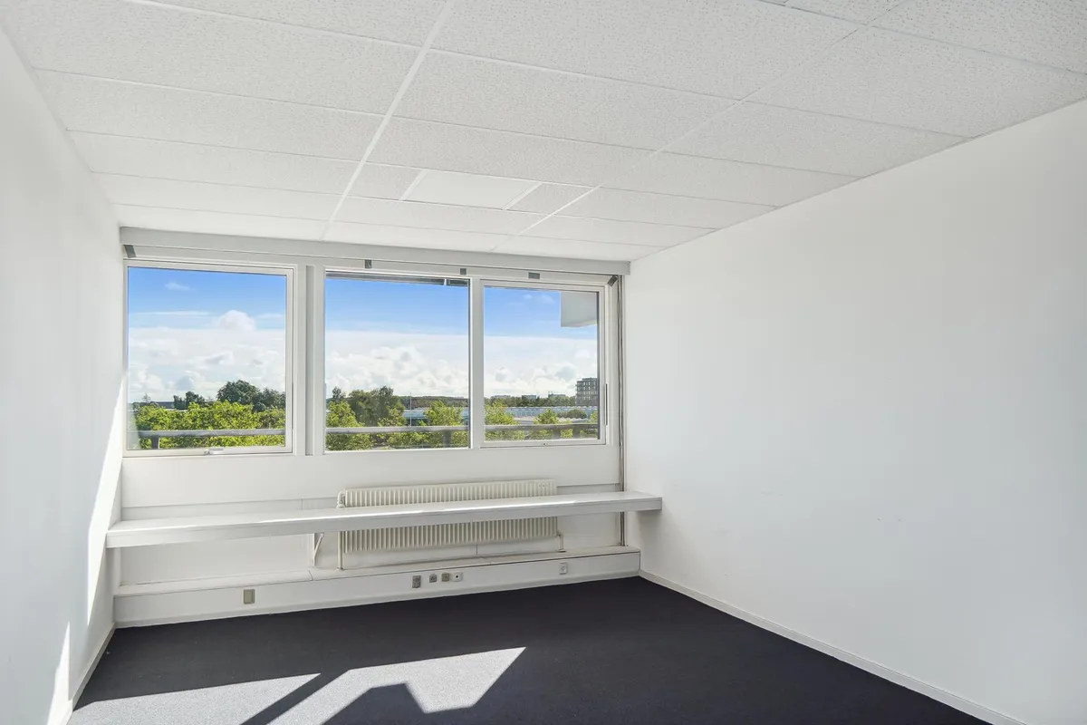 Moderne kontor med hvidt loft og hvide vægge, store vinduer, gulvbelægning og radiator under vinduet