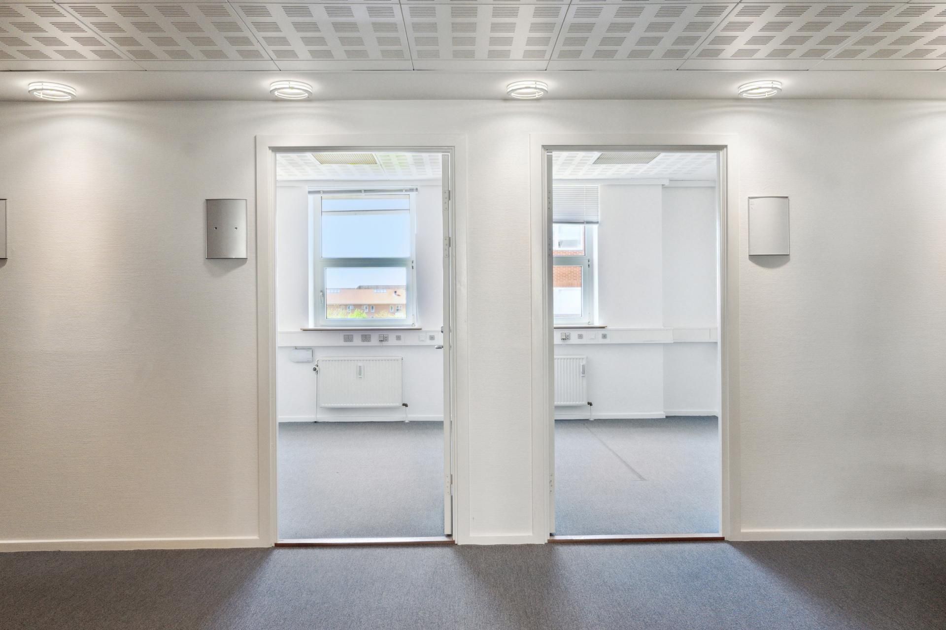 To hvide rum med hvide vægge og gulve, hver med to døre, der åbner mod hver anden. Rummene har hvide lofter med indlejrede