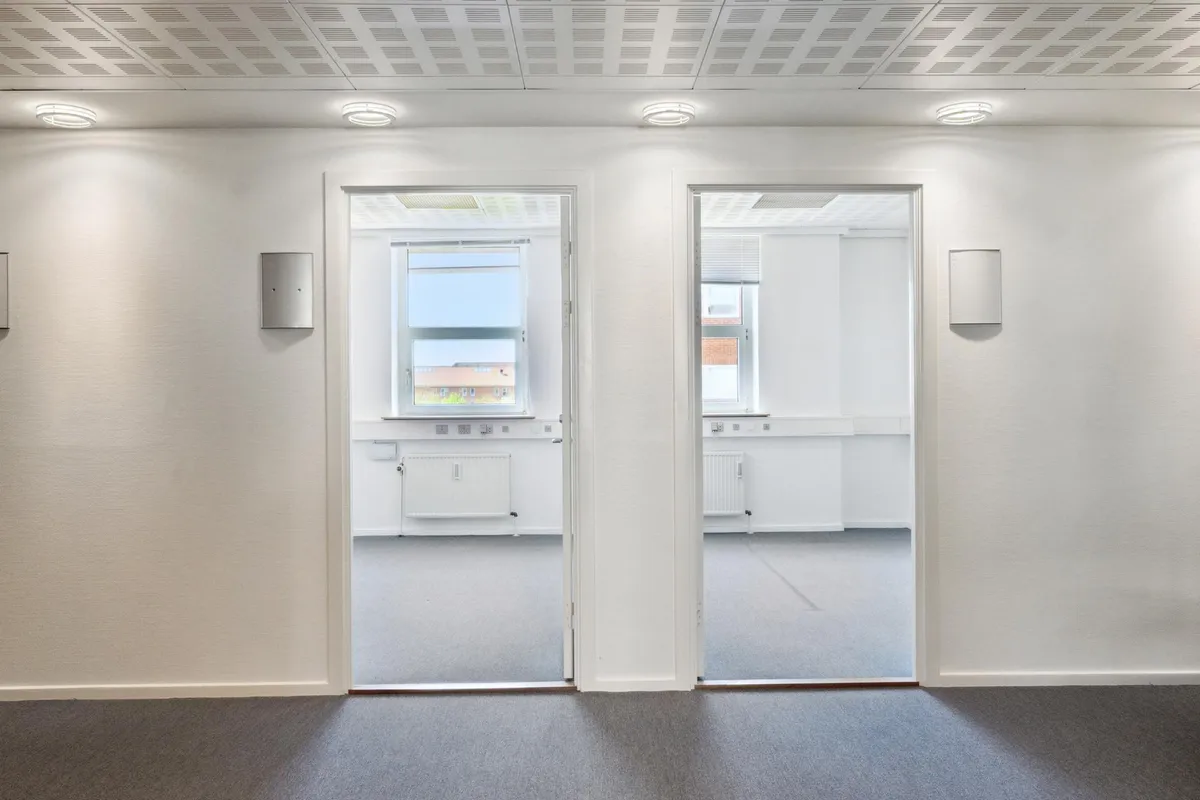 To hvide rum med hvide vægge og gulve, hver med to døre, der åbner mod hver anden. Rummene har hvide lofter med indlejrede