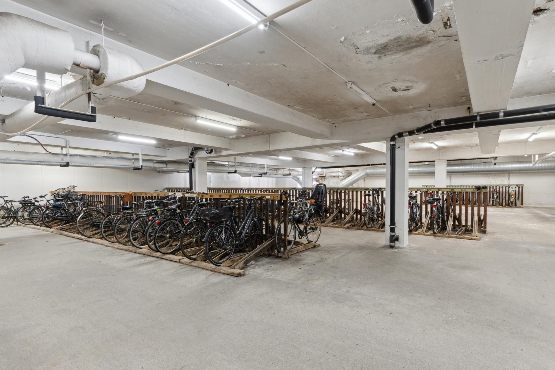 Cykler parkeret på stel på et kontorfællesskab. Mange cykler er parkeret i rækker.