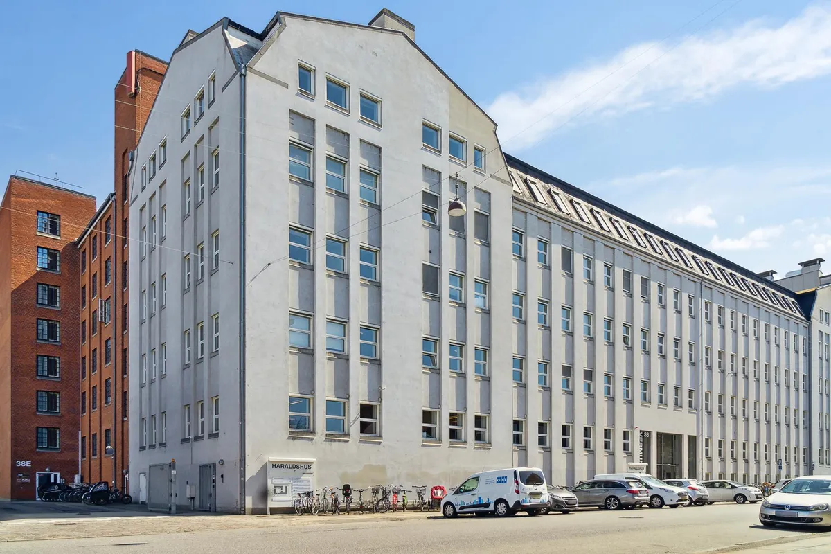 Kontorbygning med flere parkerede biler og cykler og mærket Haraldshus på facaden