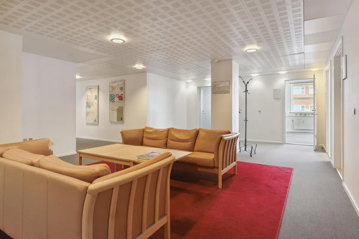 Kontorlokaler med beige lædersofaer, en træbord og et rød tæppe på gulvet i en rummelig, vellyst kontorlokal med hvide vægge