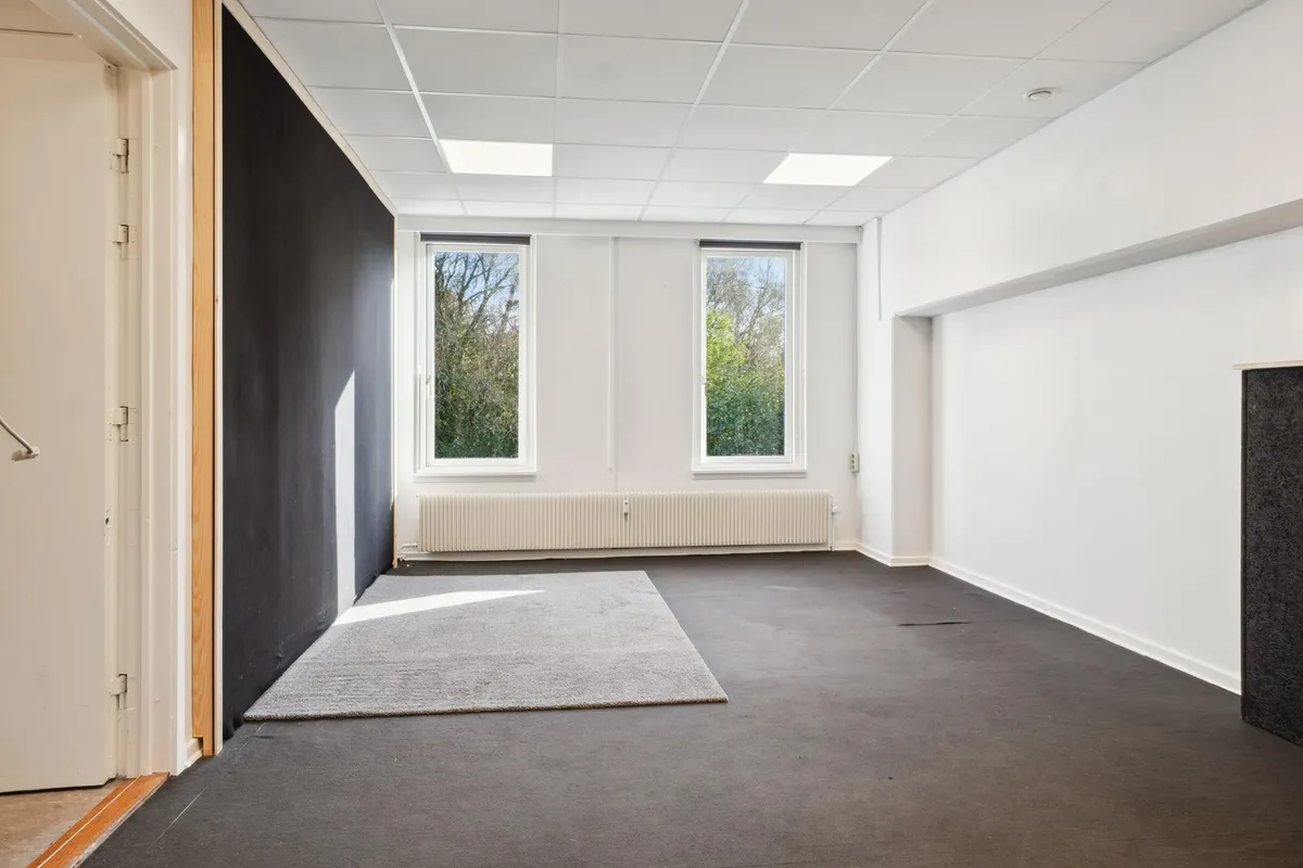 En tom og vellyst øvelokale med hvide vægge, to vinduer og en lysegrå gulvmåtte
