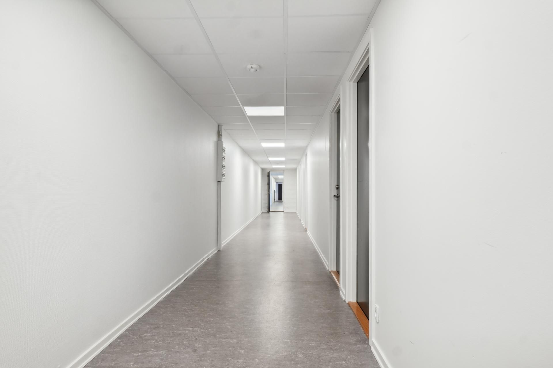 Kort og lys hall med hvide vægge og gulv og tærskler med mørke døre til højre og venstre