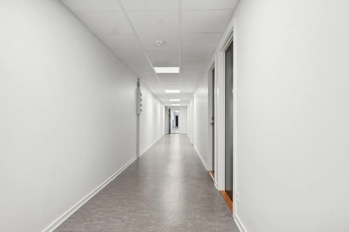 Kort og lys hall med hvide vægge og gulv og tærskler med mørke døre til højre og venstre