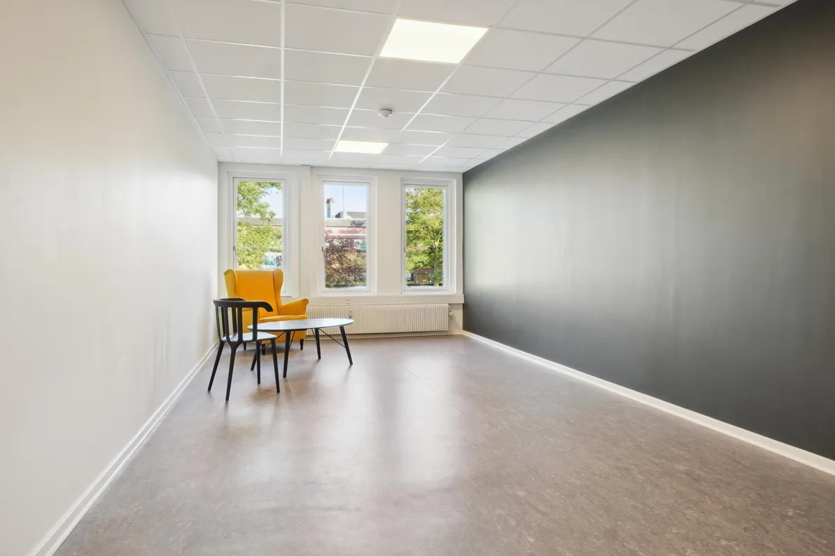 En stor og rummelig øvelokale med hvide vægge, gulv og loft, samt en sort væg og lyse gulve.