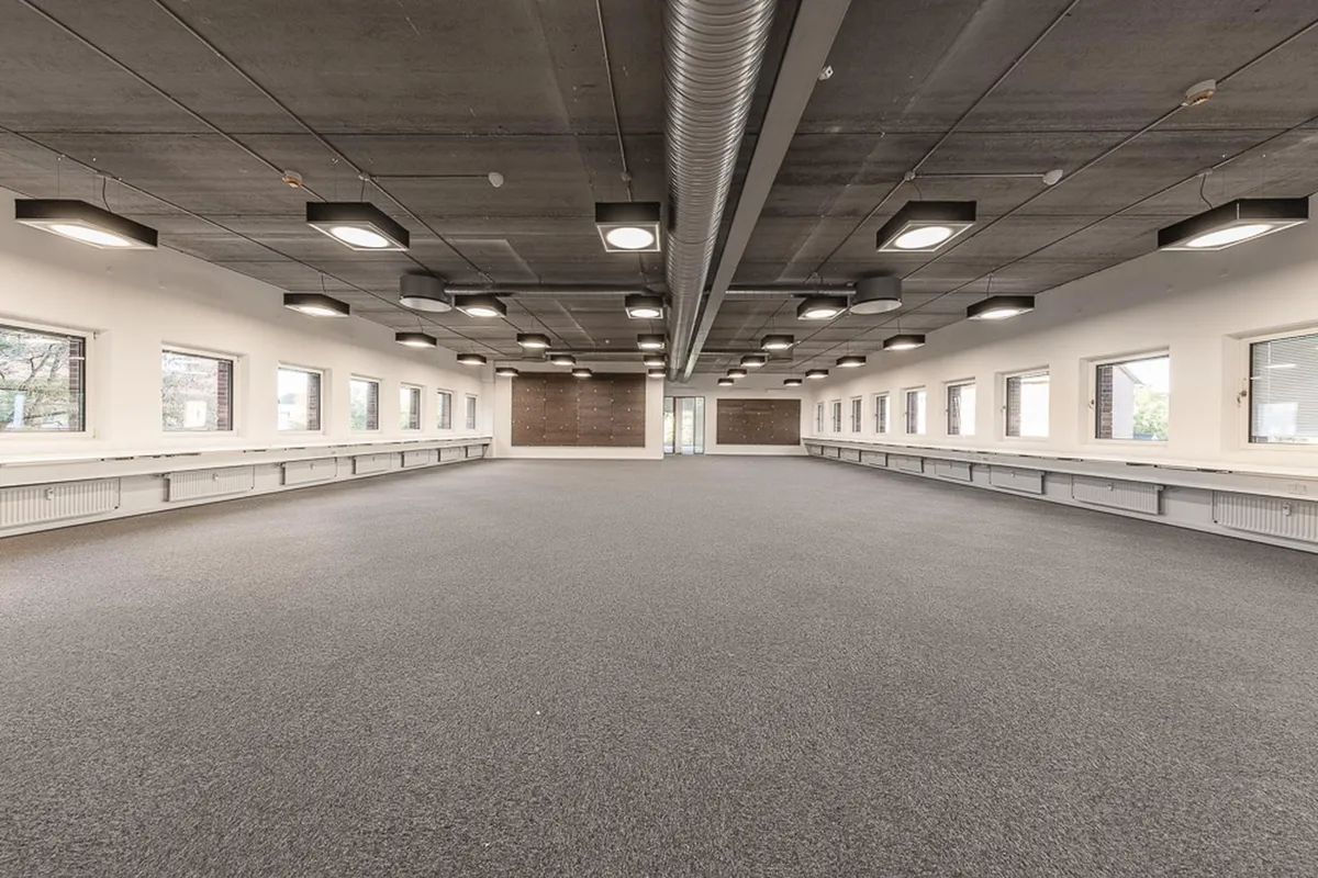 Kontor med lyse loftslampe og store vinduer i Kgs. Lyngby, idet man kan se et tomt gulv og møbler langs væggen