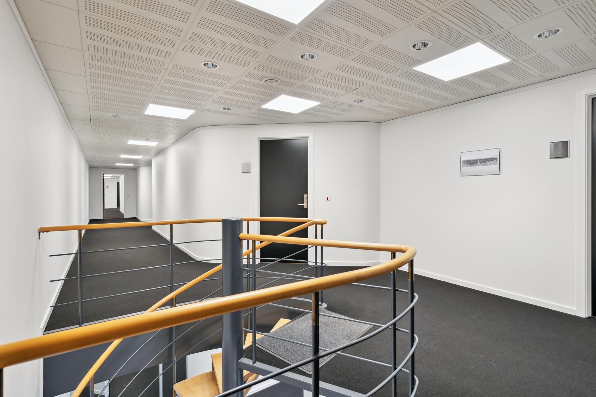 Et økologisk designet indre af et erhvervscenter med moderne hvid og guldtreppe, lyse loftsplader og en slank møbelstil.