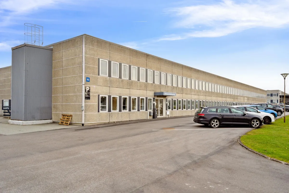 Forretningsbygning med parkeringsplads foran, hvor biler er parkeret, og der er en skulptur på taget