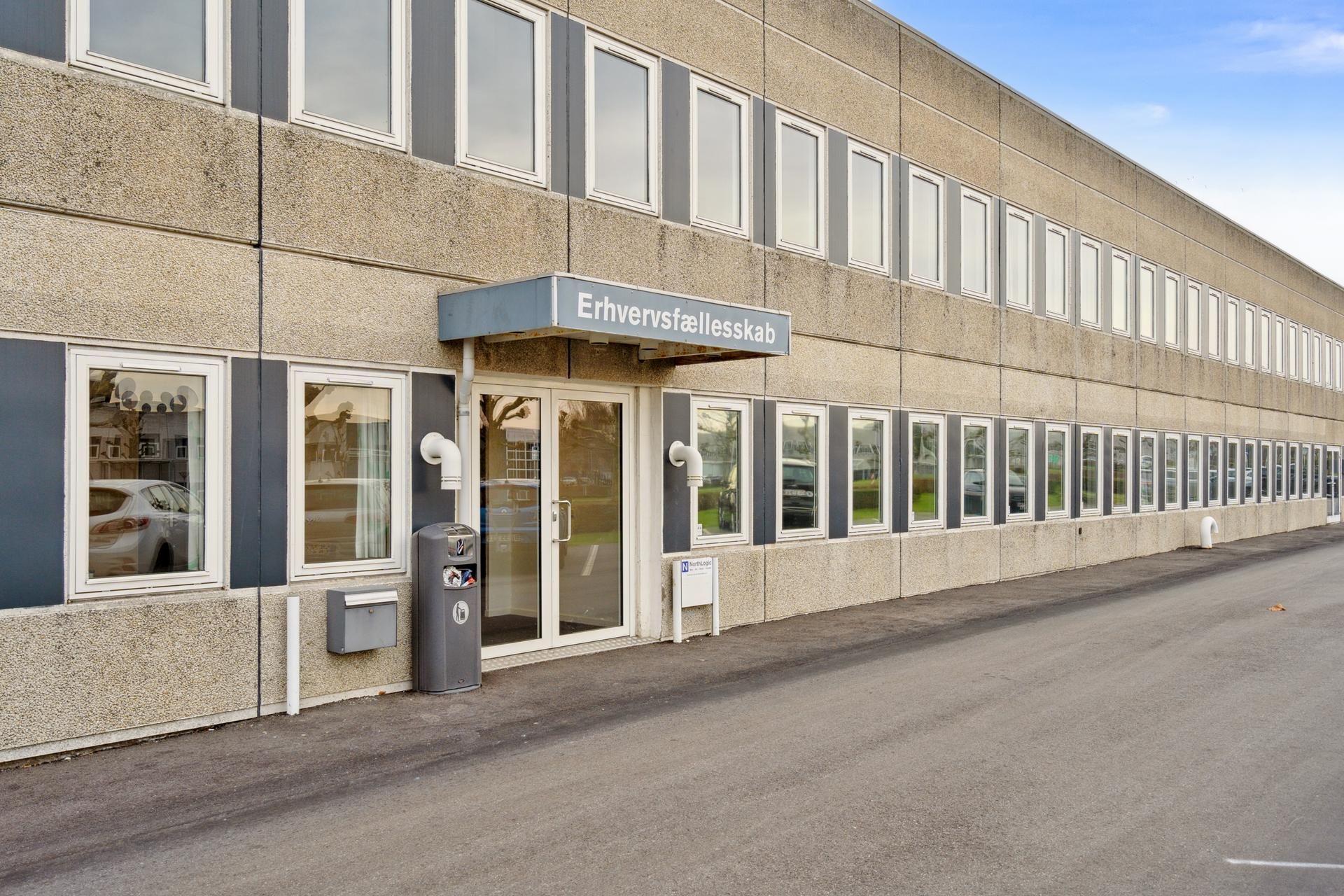 Et erhvervscenter med flere vinduer og døre, hvor en skravet er markeret med "Ervhervsfællesskab" og der er placeret en