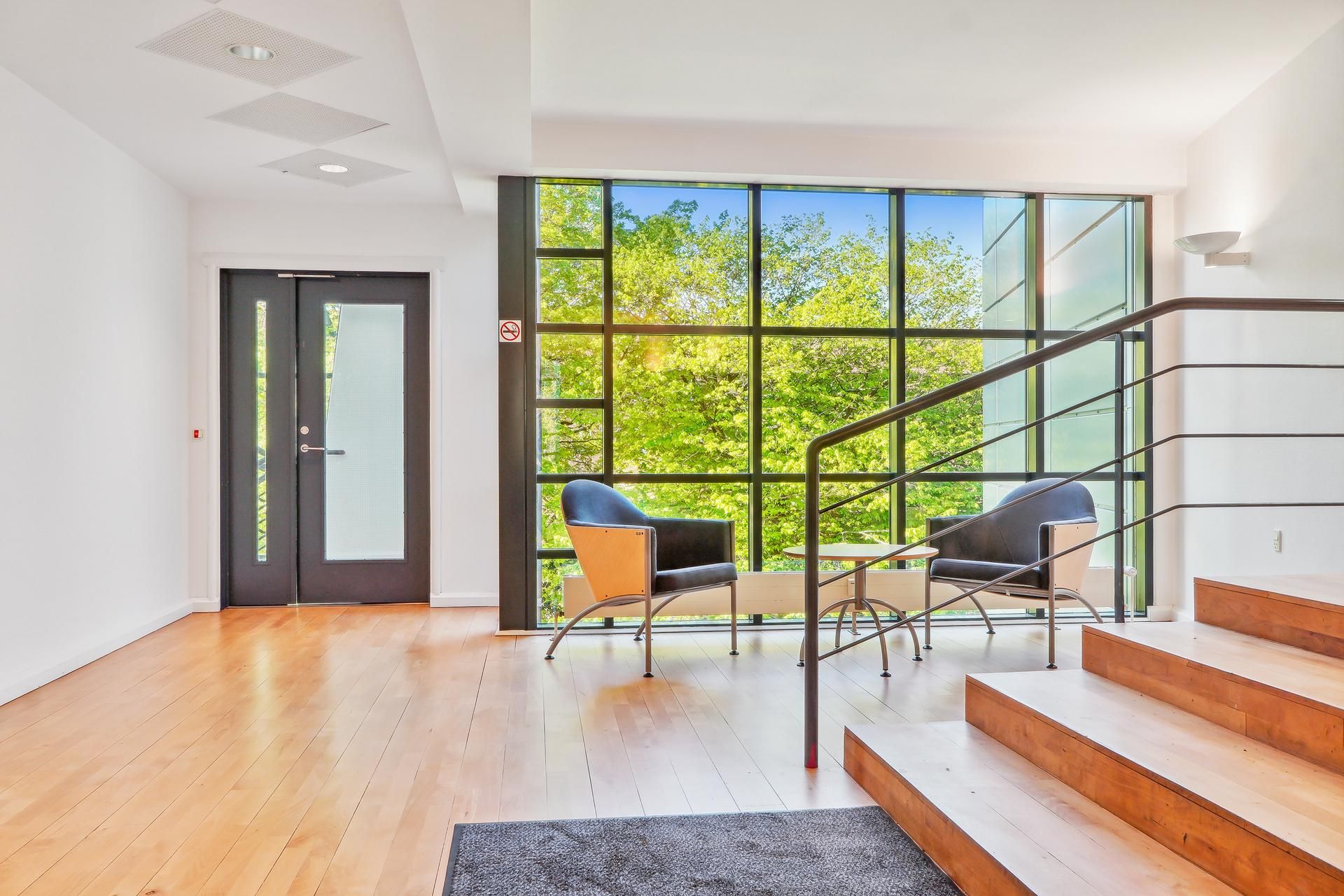 Moderne og lys indgangszone med trægulve, mørkelæggende gardiner og lyse vinduer samt to stolpe og stige