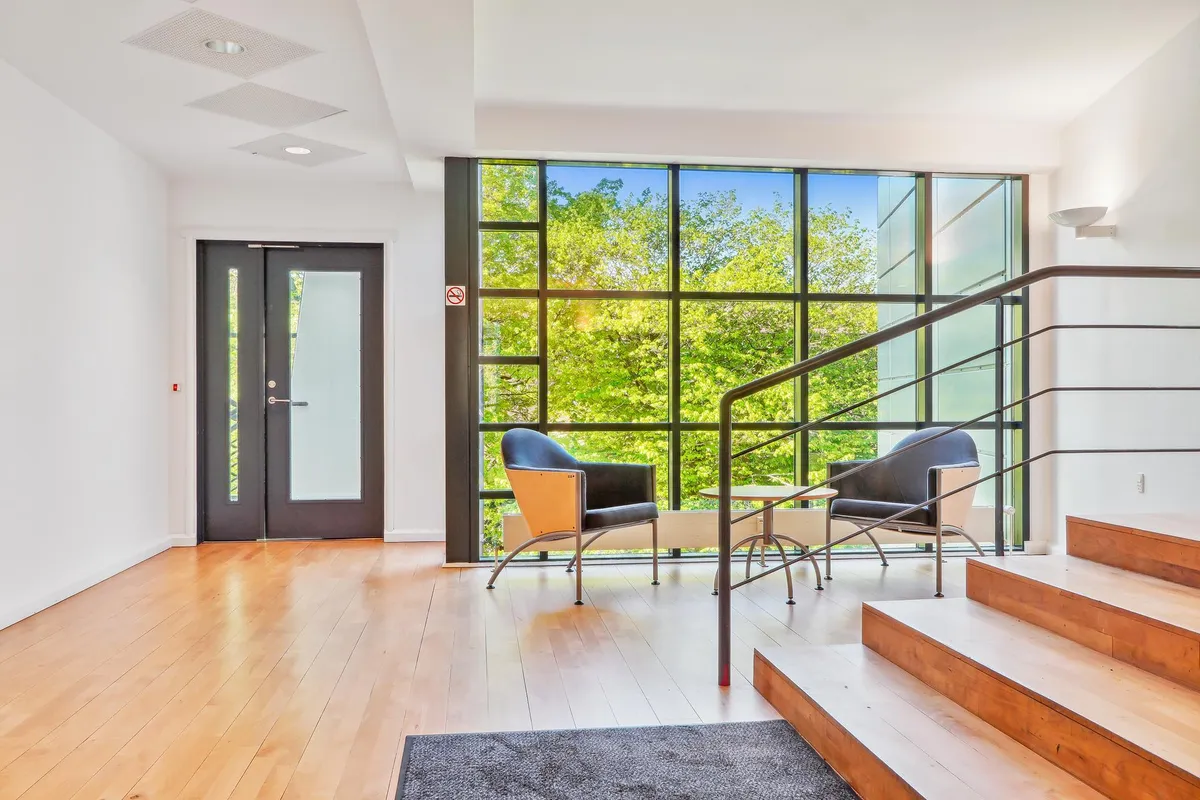 Moderne og lys indgangszone med trægulve, mørkelæggende gardiner og lyse vinduer samt to stolpe og stige