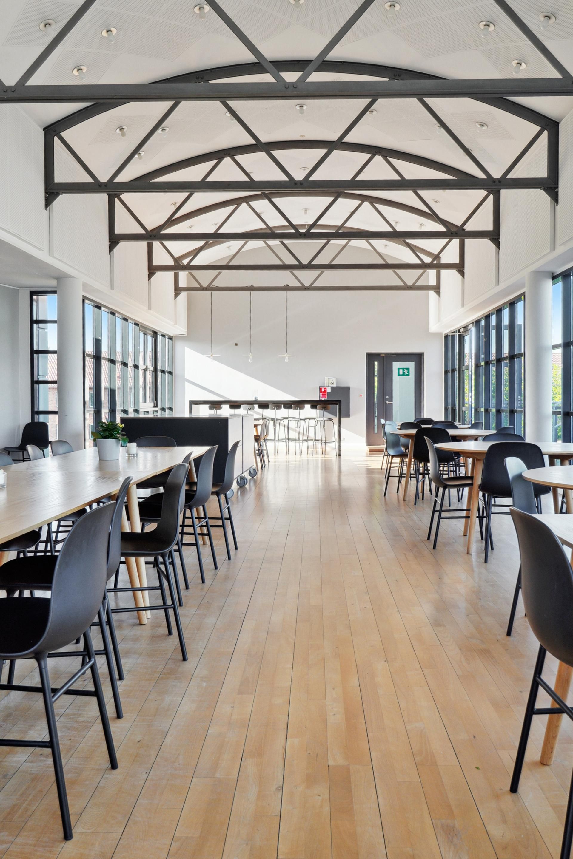 Stort kontor med højt loft, trægulve, moderne møbler og glasvinduer med udsigt til gaden