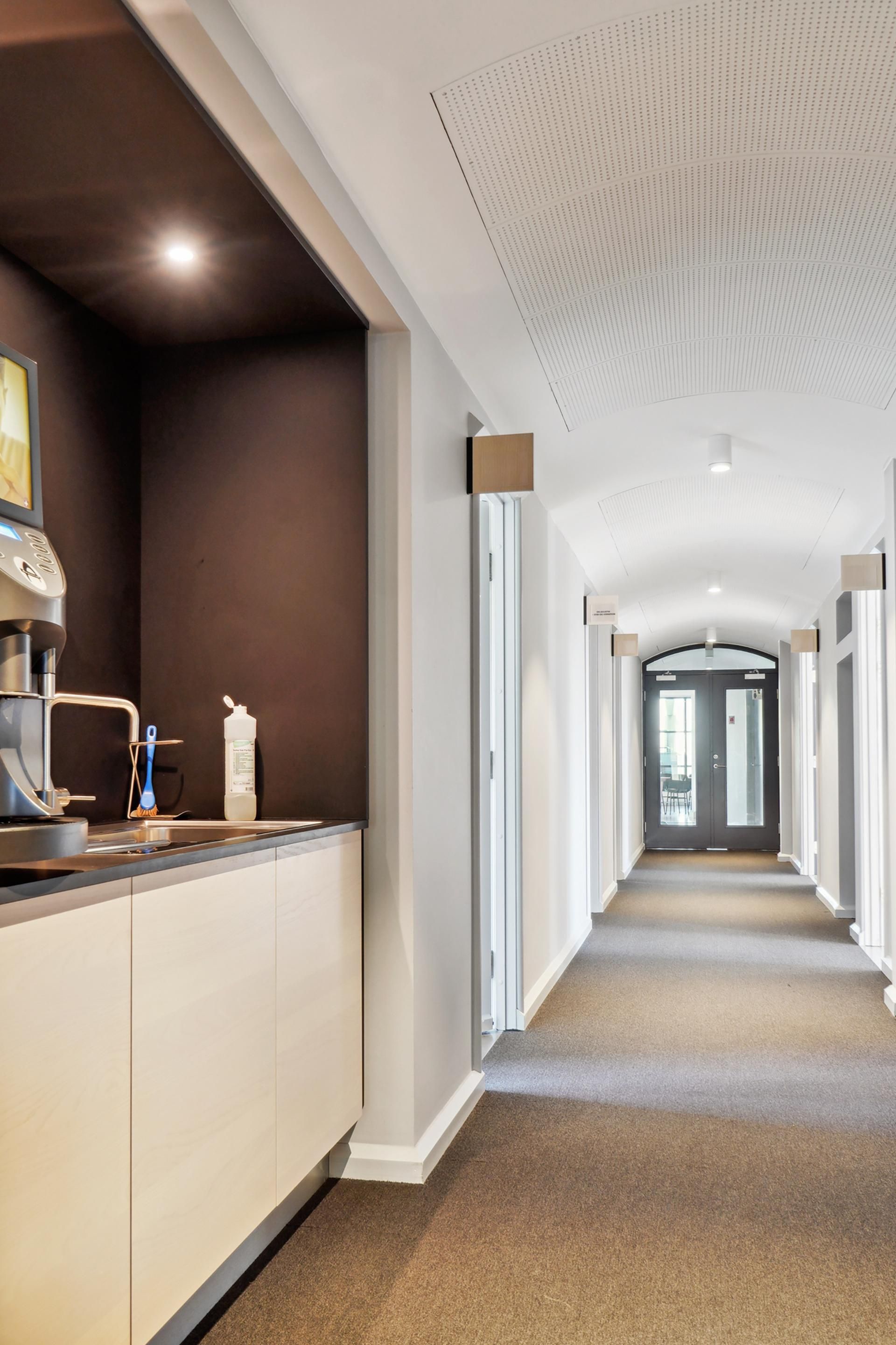 Kontor med en kaffemaskine, en børste, en flaske og en sænket loft i en række med hvide vægge