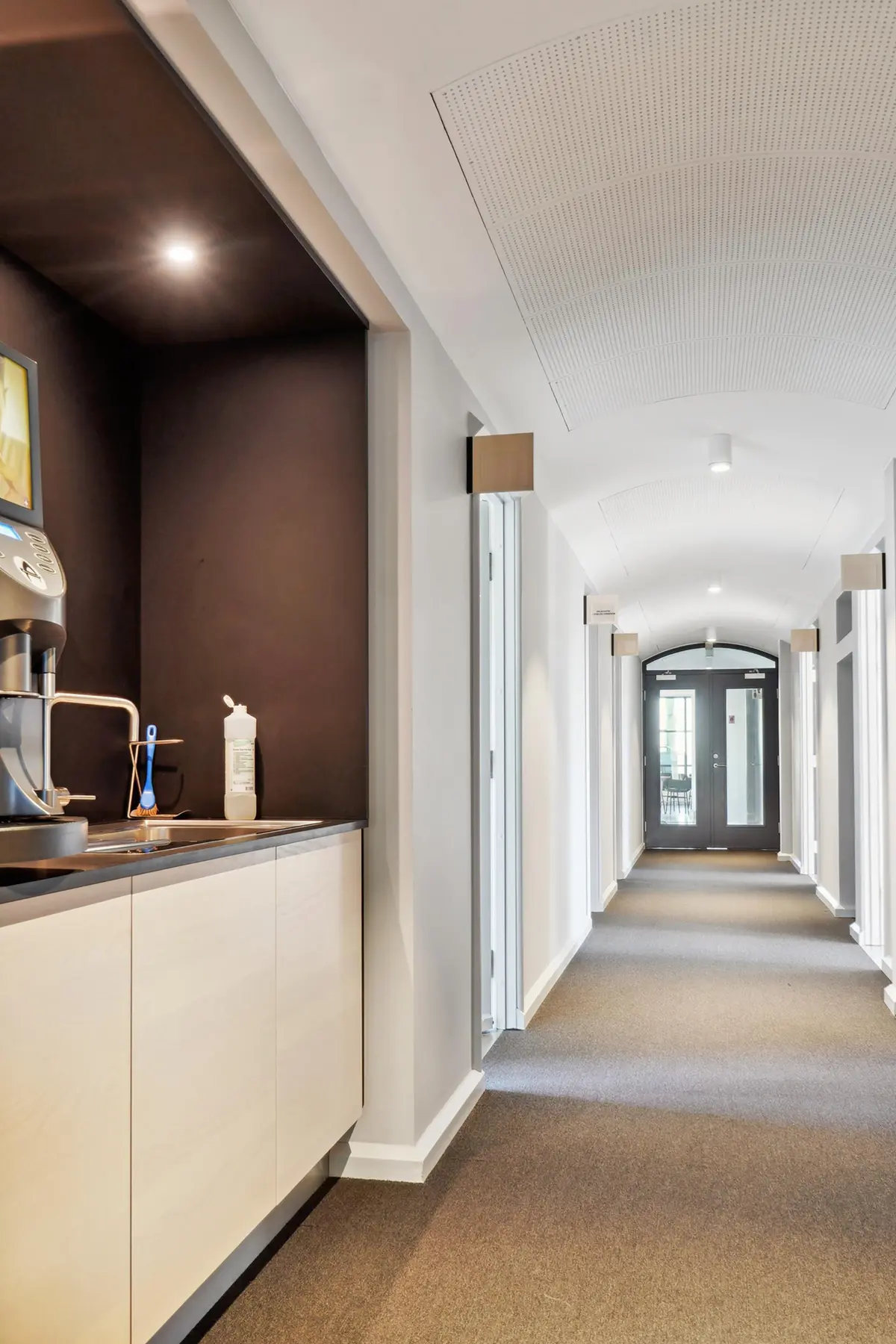 Kontor med en kaffemaskine, en børste, en flaske og en sænket loft i en række med hvide vægge