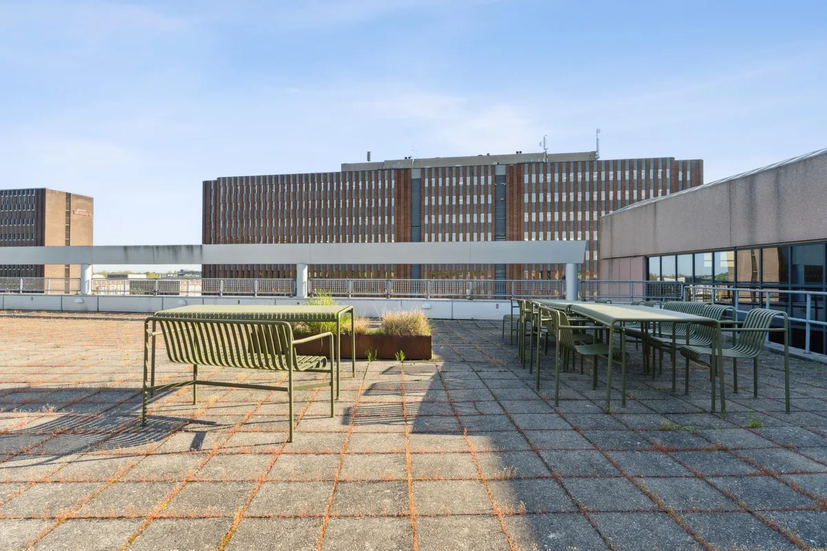 Kontorfællesskab med grønne stole og borde på taget, en bygning med glasvinduer og røde mursten