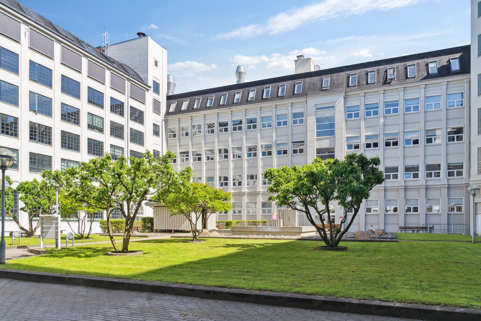 Moderne bygning med glasvinduer, solceller og grønne træer i en byggefællesskab på Østerbro