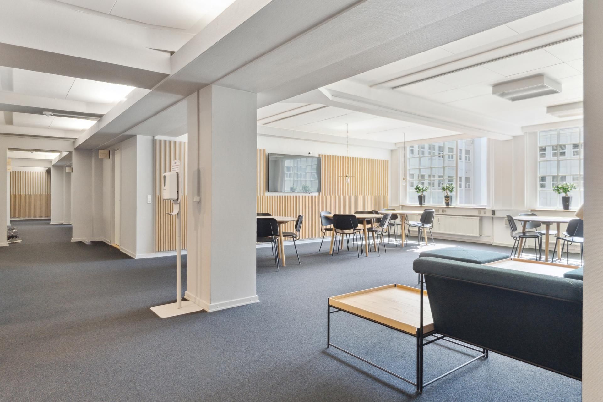 Moderne kontorfællesskab med hvide lofter og gulv, lange runde borde, lyse og rene møbler samt vinduer med udsigt til