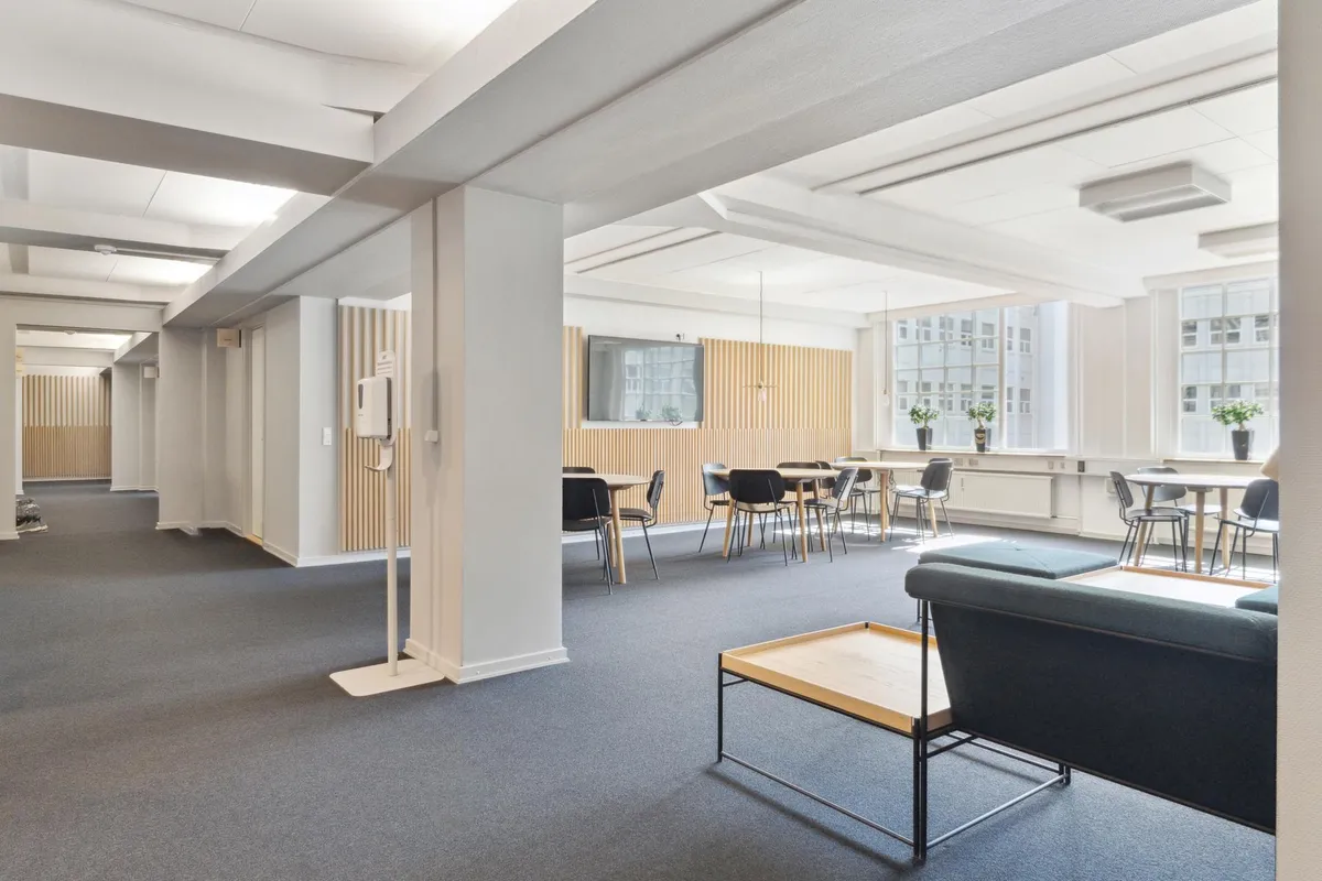 Moderne kontorfællesskab med hvide lofter og gulv, lange runde borde, lyse og rene møbler samt vinduer med udsigt til