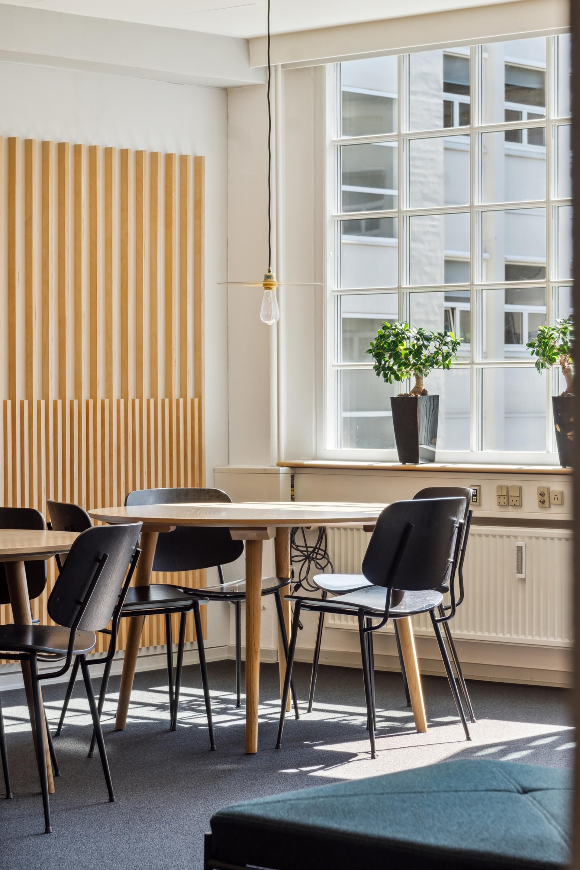 Inde i kontorfællesskabet er der et lyse og moderne mødelokale med lyse trævægge og et elegant bord med fire stolpe uden