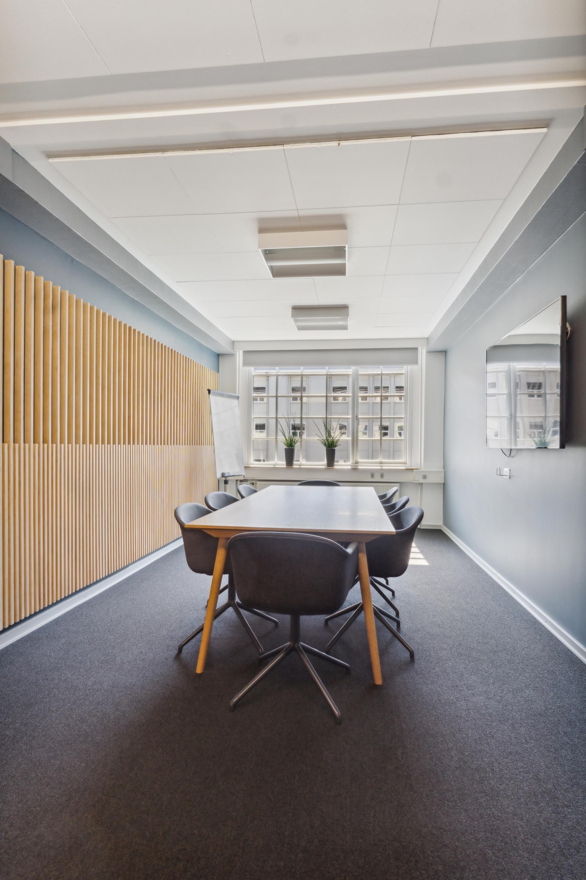 Kontor med bord, stole og hvide vægge samt et whiteboard og plantepoter på vindueskarmen