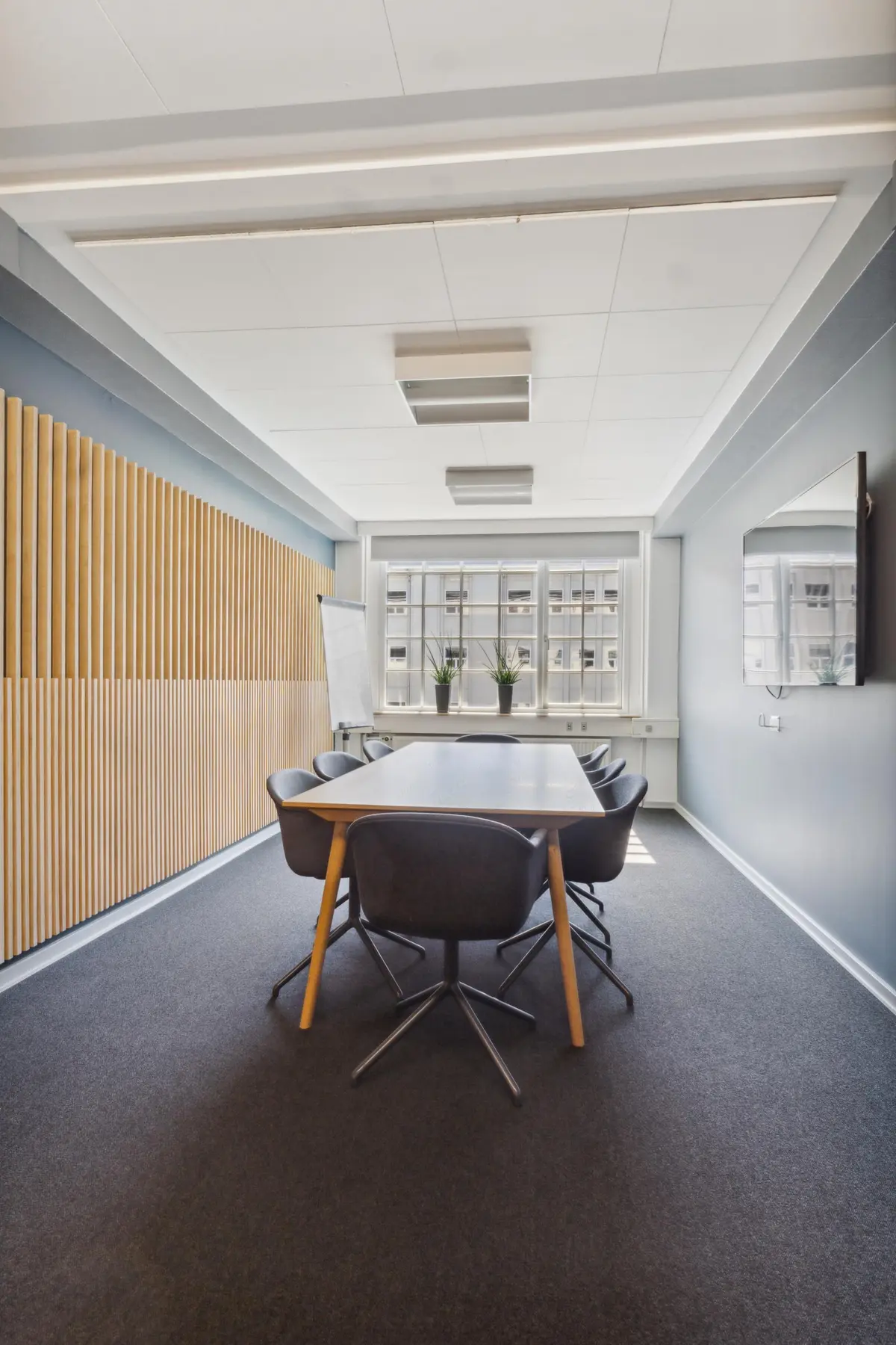 Kontor med bord, stole og hvide vægge samt et whiteboard og plantepoter på vindueskarmen