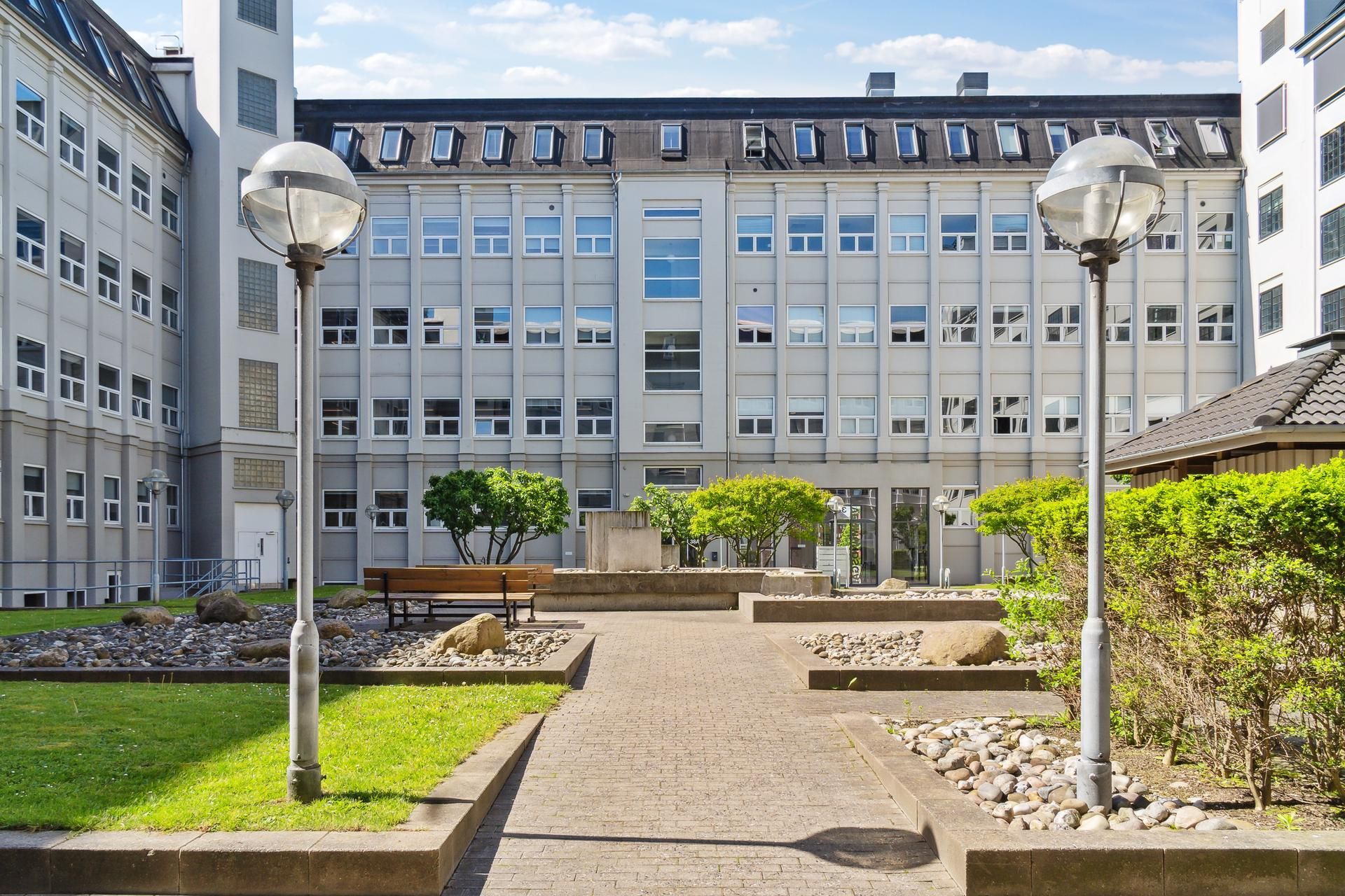 Kontorfællesskab med gårdhave og grønne planter samt lyse vinduer og lysekroner.