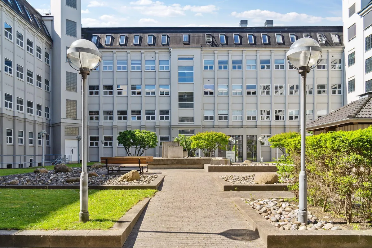 Kontorfællesskab med gårdhave og grønne planter samt lyse vinduer og lysekroner.