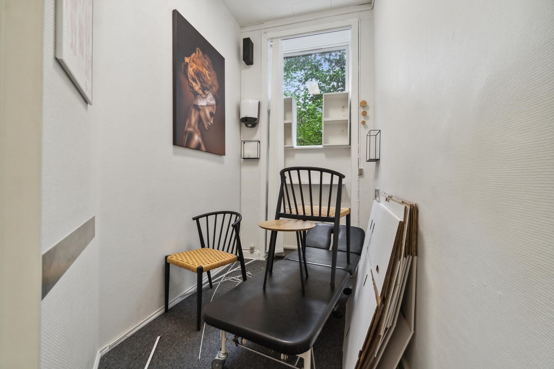 Lejlighed med lyse, smukke vægge og moderne møbler, herunder stol, bord og senge, og lyseruder med udsigt til grønne træer