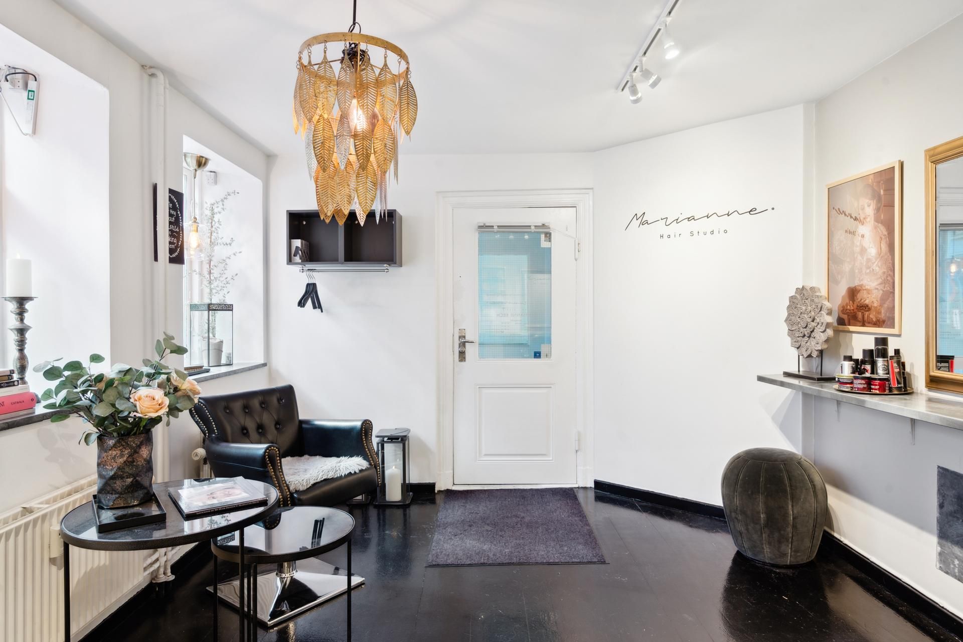 Marianne Hair Studio i København med sofa, tavle, plante og lysekroner på loftet