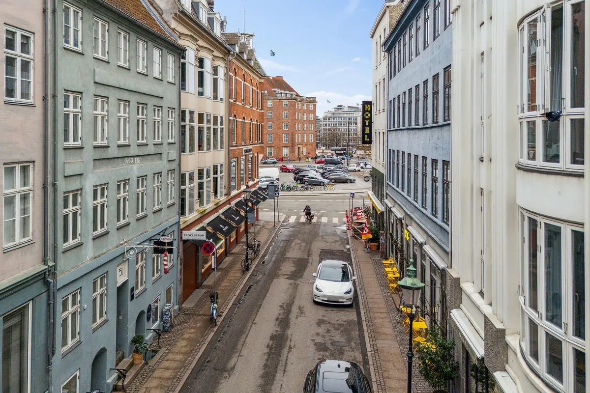 En bil kører langs Sankt Peders Stræde i København, og en cykelkører krydser midt på gaden