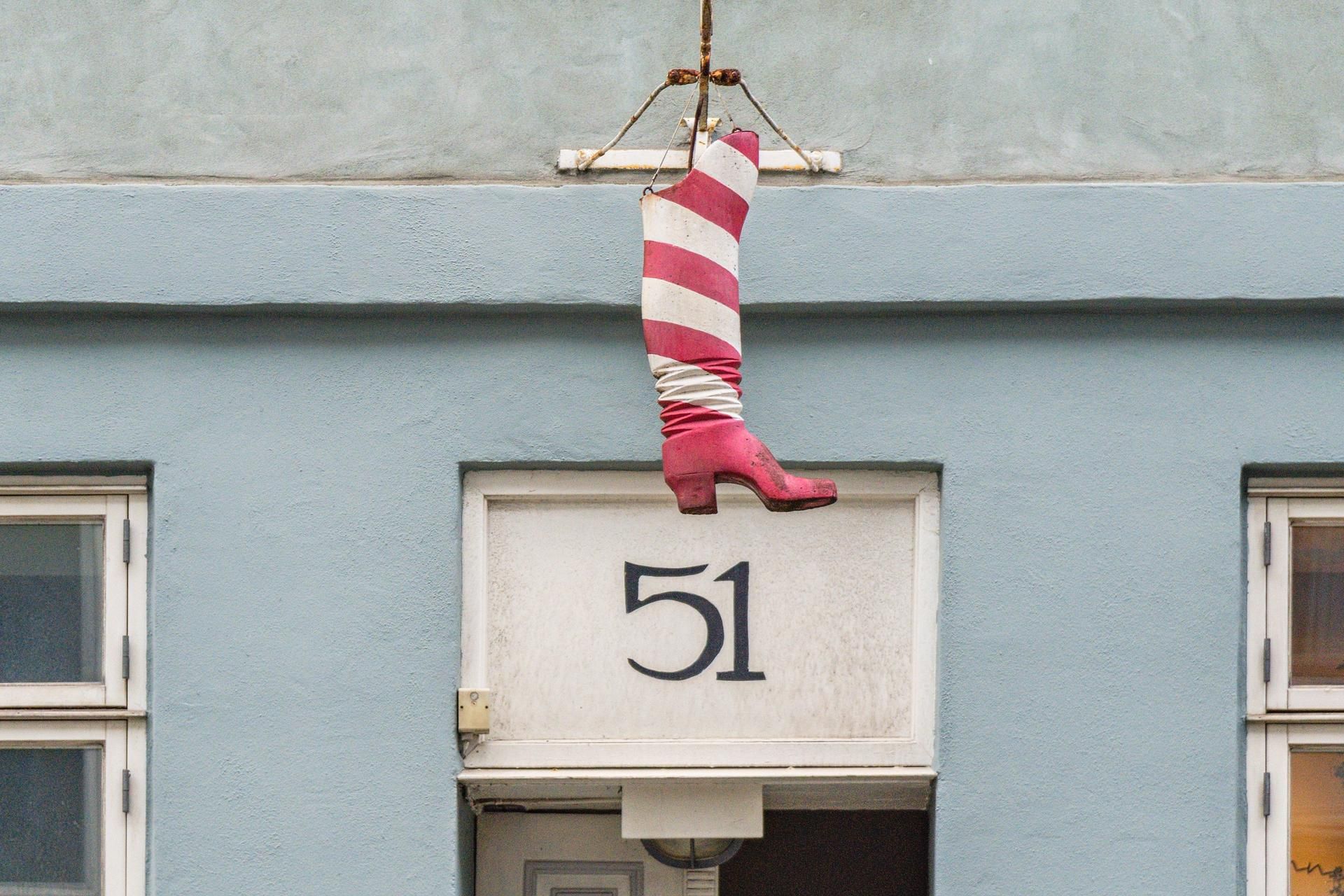 Hængende rødt og hvidt stribet støvle på et blåt bygningsnummer 51 i København. Butiksdør med nummer 51 og rødt og hvidt