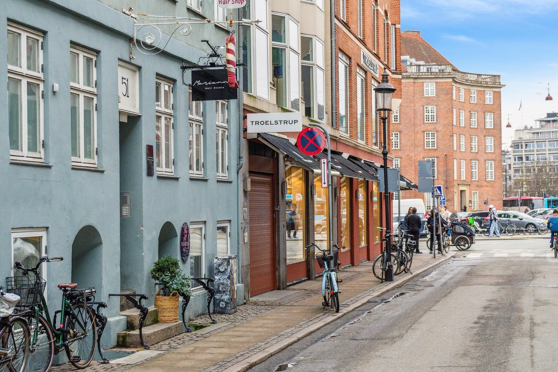 Butikker og cykler parkeret langs gaden, og en rødmalet cykelskilting med påskriften Troelstrup