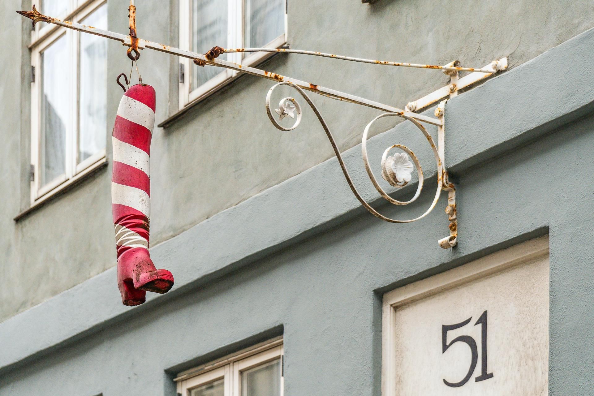 En rusten metalbøjle med en rødt og hvidt stribet højsko hængende fra den og en nummerplade med tal 51 på en blå mur i