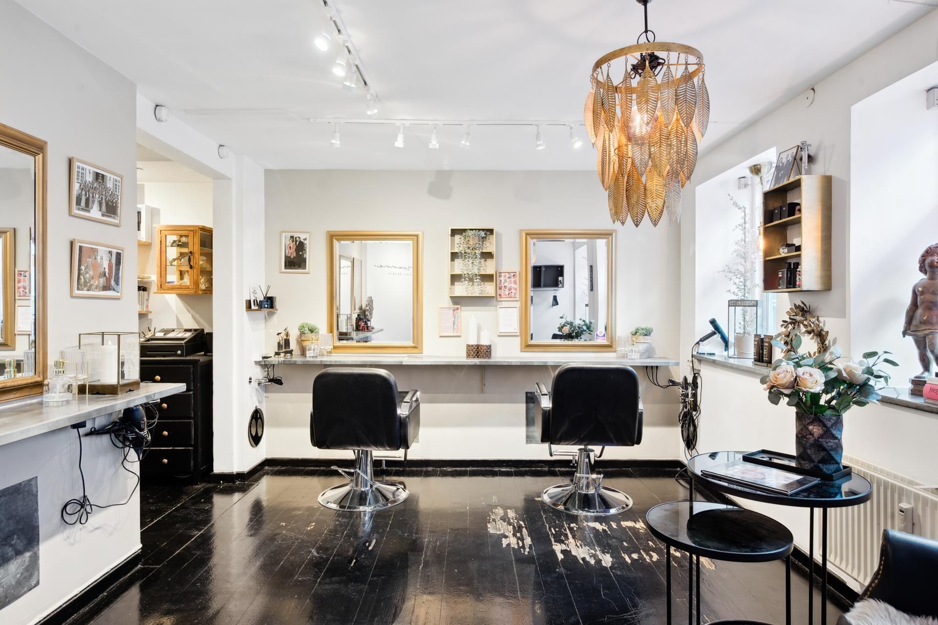 To barberstole i et moderne interiør med spejle og plante i potte og et gulv med gulvet med søm og en lampeskærm med blade.