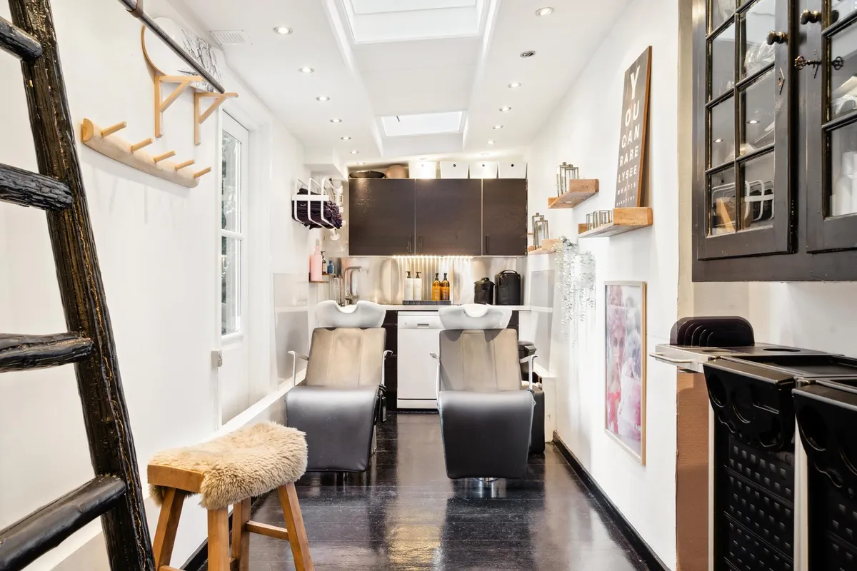 Et moderne køkken med hængende hylder og lyse loftsvinduer med to barberstole og en høj bænk i baggrunden